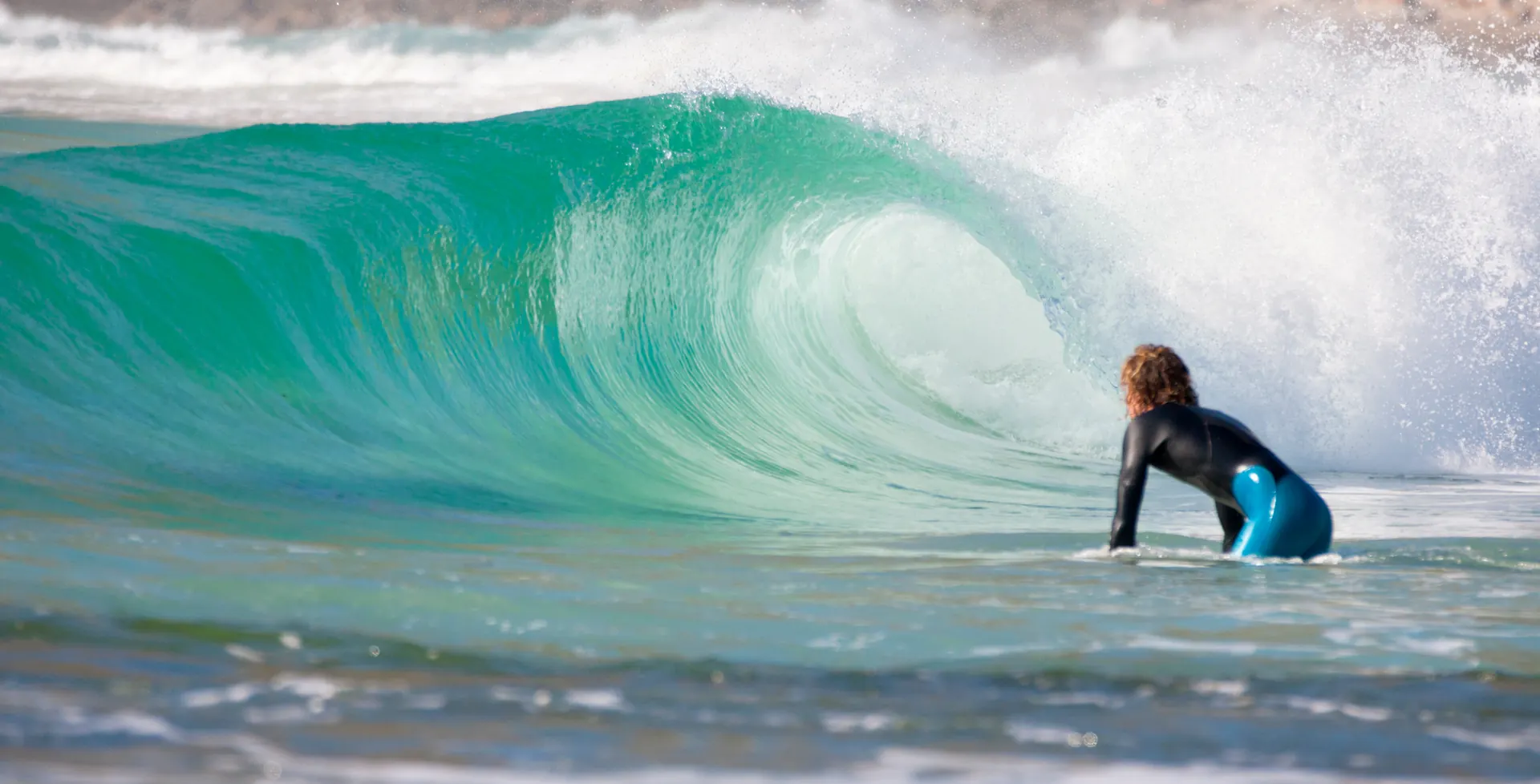 Surfer paddling out beside a breaking turquoise wave