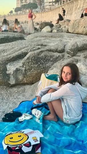 A girl sitting on a blue HAMI beach blanket among the boulders at a Cape Town beach