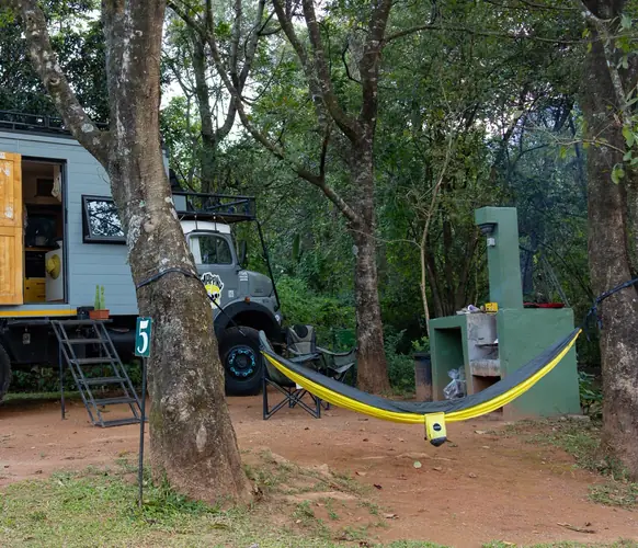 A yellow HAMI hammock strung between trees at a bush campsite, next to an overland truck